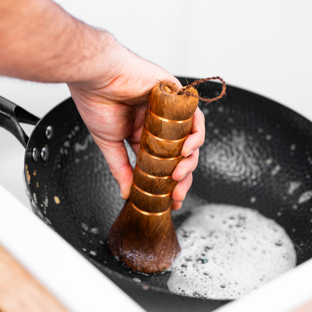 Le Pakia Wok-Reinigungsbürste aus Pflanzenfasern beim Reinigen des Woks in der Hand