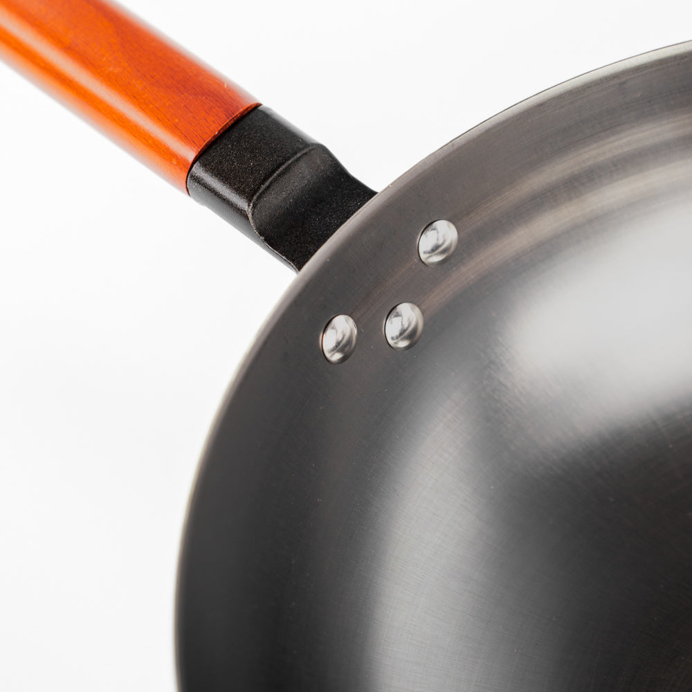 Le Oniri Wok 32 cm aus Gusseisen mit Holzgriff in der Hand gehalten